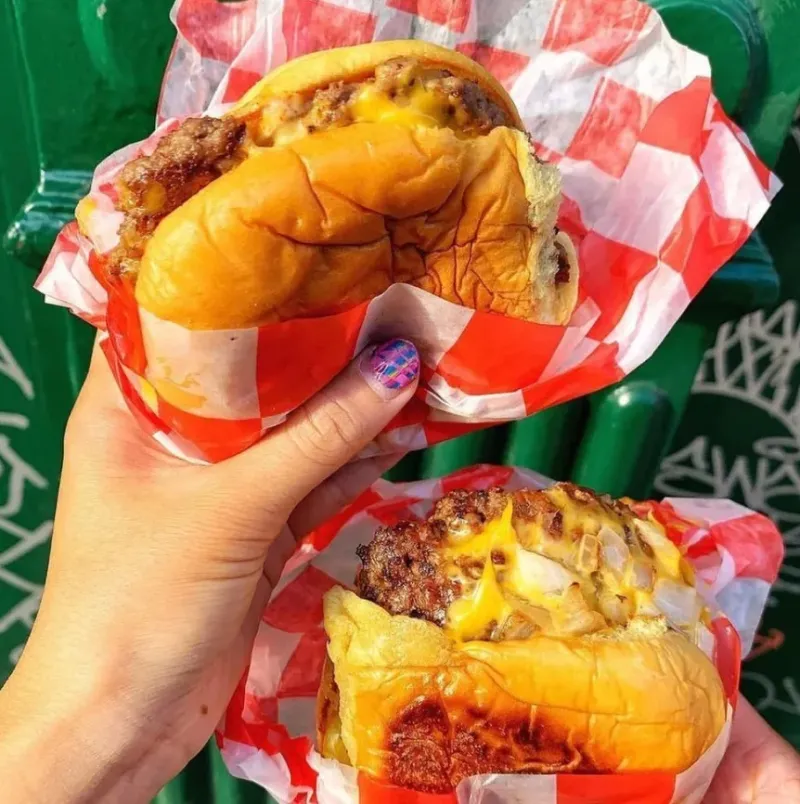 Two 7th Street Burger cheeseburgers held outdoors in branded burger wrappers