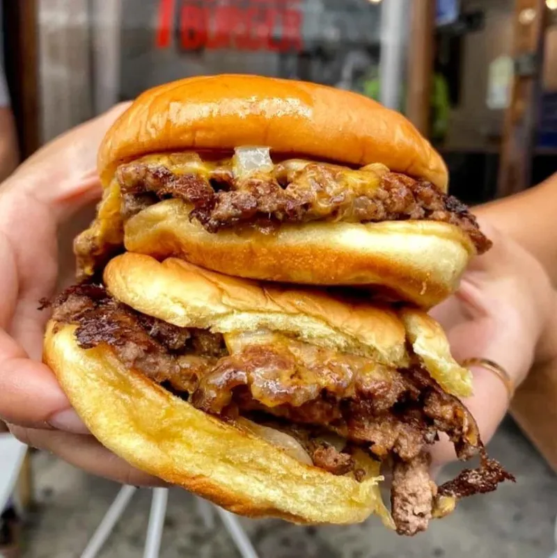 Two 7th Street Burger cheeseburgers held outside a restaurant storefront