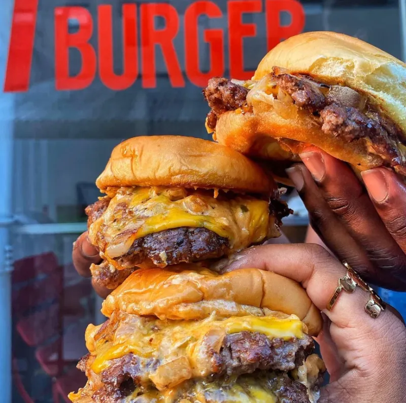 Three 7th Street Burger cheeseburgers held outside a restaurant storefront