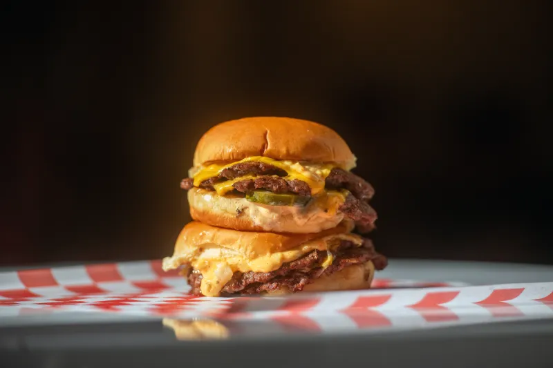 Two stacked 7th Street Burger double cheeseburgers with American cheese, pickles, and house sauce